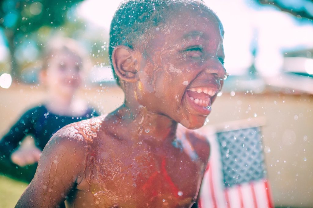 happy laughing black boy running through sprinkler