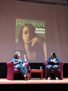 two Black women on stage seated in chairs talking to each other