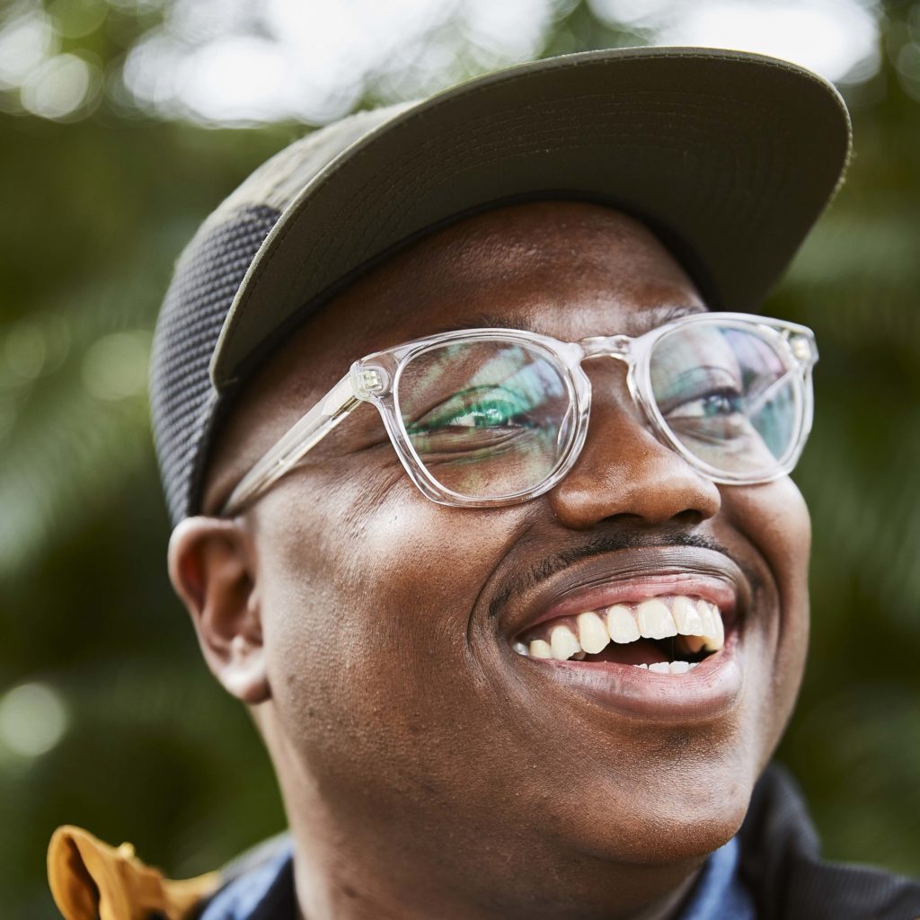 smiling young Black man wearing glasses and baseball cap and looking to side