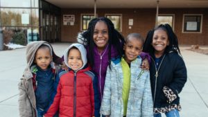 5 black kids smiling in front of school