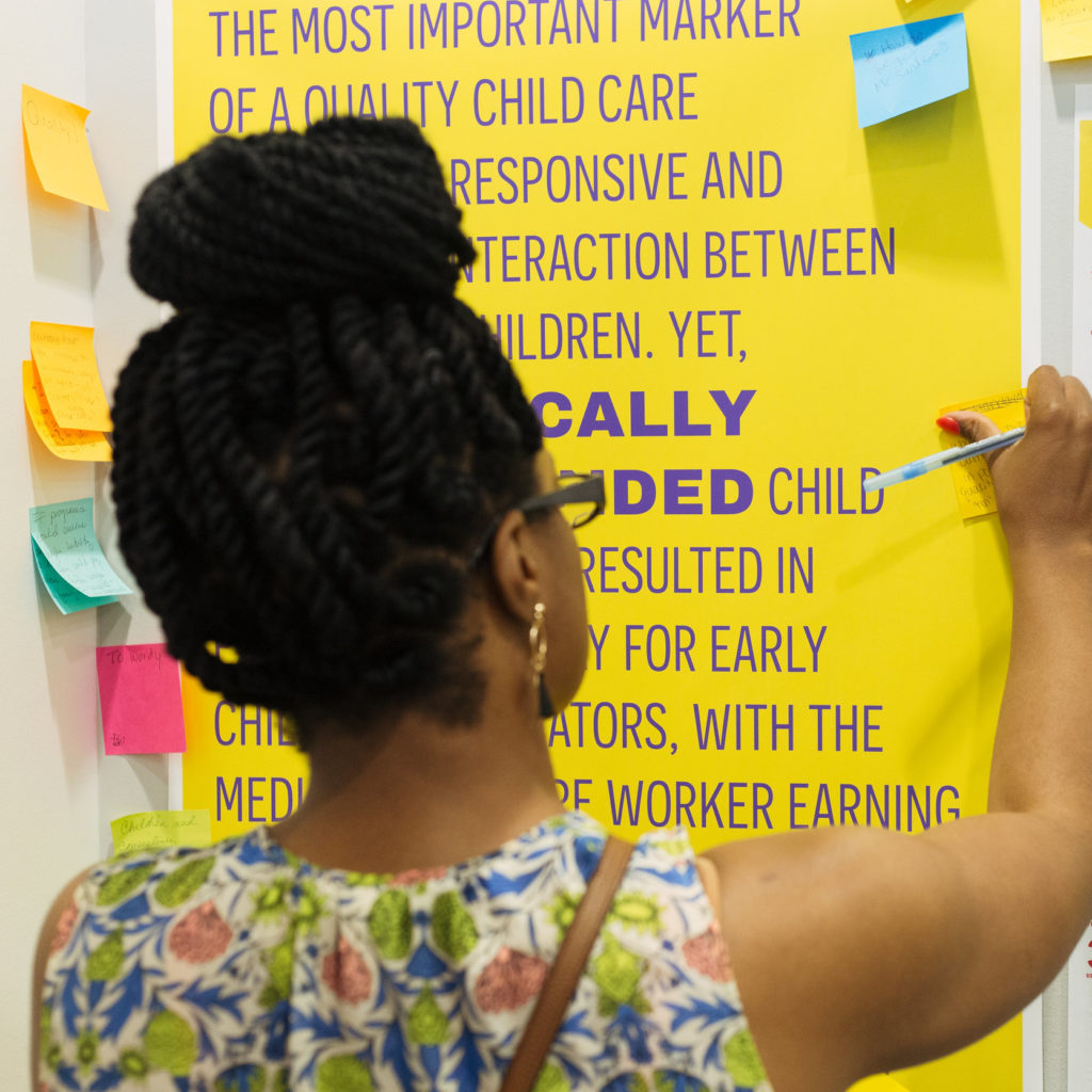 Black woman placing sticky note on poster on wall