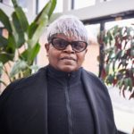 Determined older black woman with short purple and grey hair wearing glasses