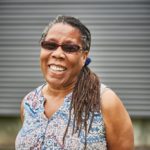 Grinning older Black woman with sunglasses and long braids