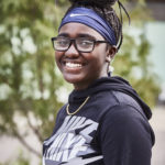Grinning young Black woman with glasses, long braids held up by headband