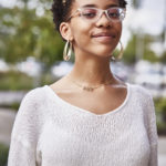 Young Black woman with glasses grinning confidently