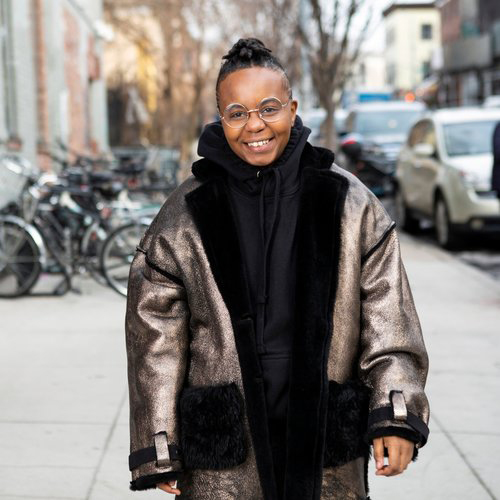 A transmasculine Black person in a winter coat+on the sidewalk