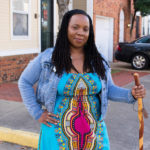 Smiling black woman with long braided hair holding walking stick