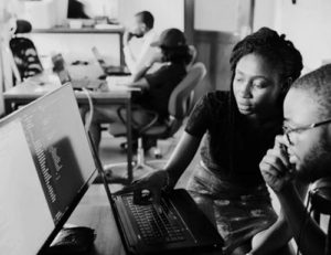 Black man and Black woman looking at computer with peers in background