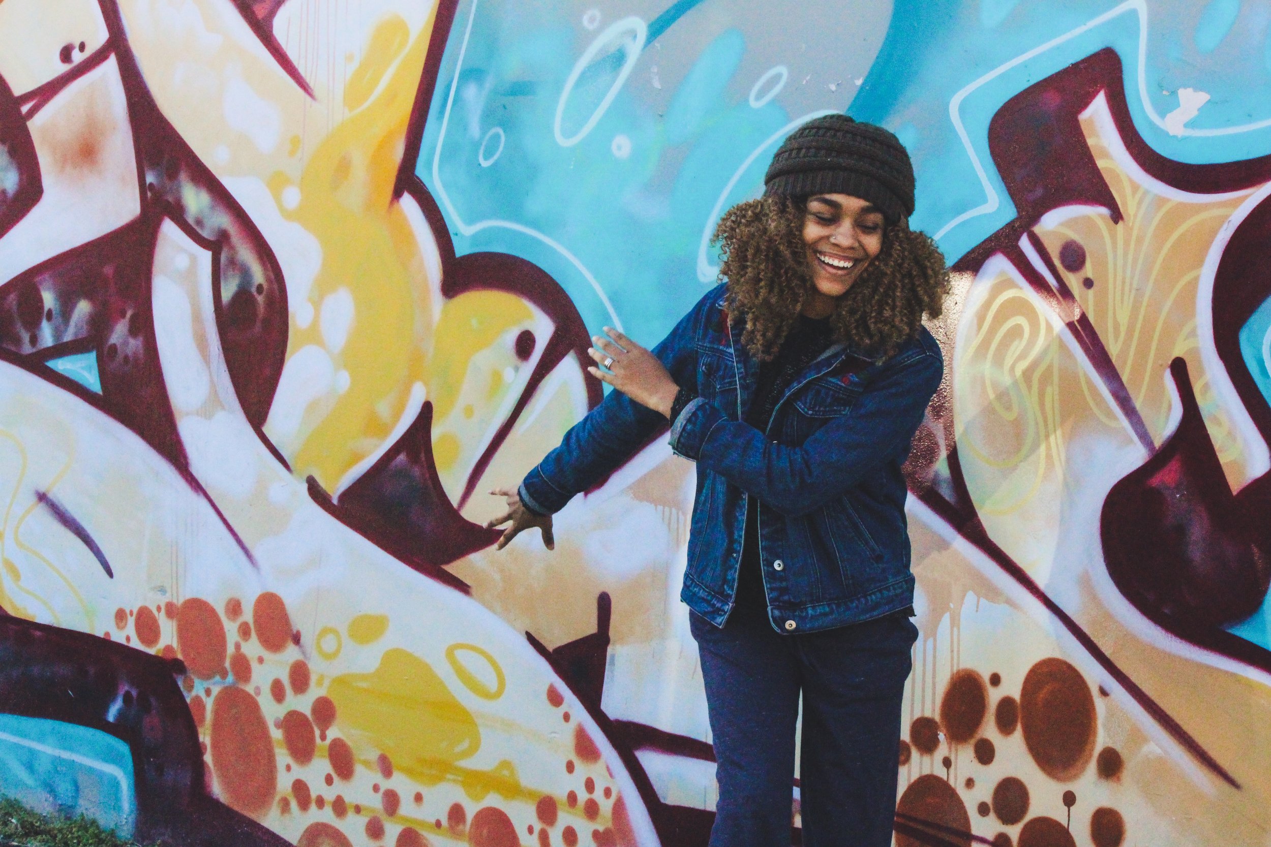 Young Black woman laughing in front of graffiti wall
