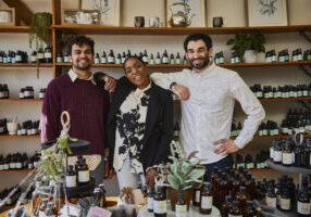 Meet the Community Wealth Building team: Edgar Payano, Keisha Maybry Haymore, and Yoni Blumberg. The team poses among the plants and tinctures of one of their entrepreneur alum’s shops, Cheryl’s Herbs. Photo by Izaiah Johnson.